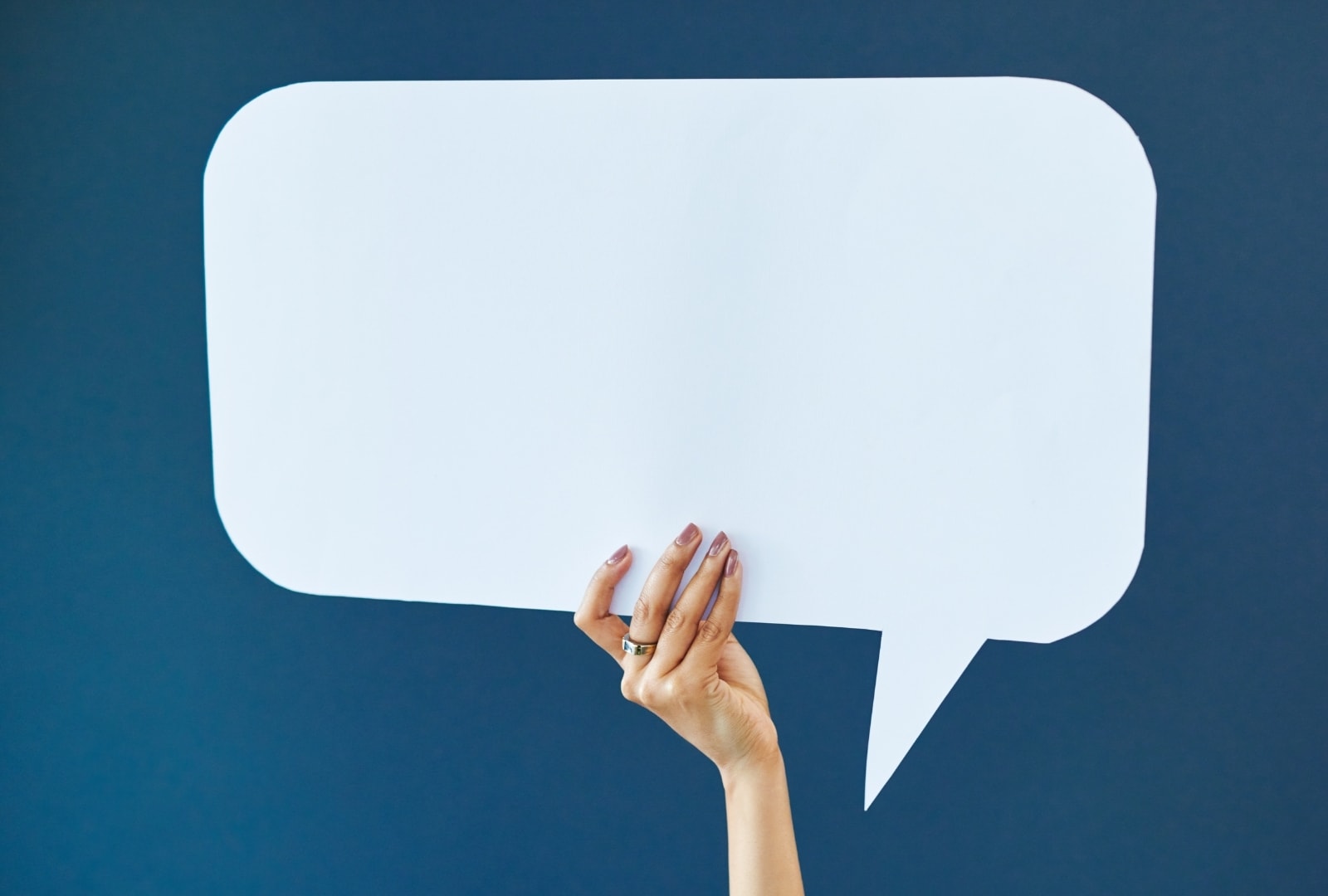 A hand holding up a large blank speech bubble against a dark blue background
